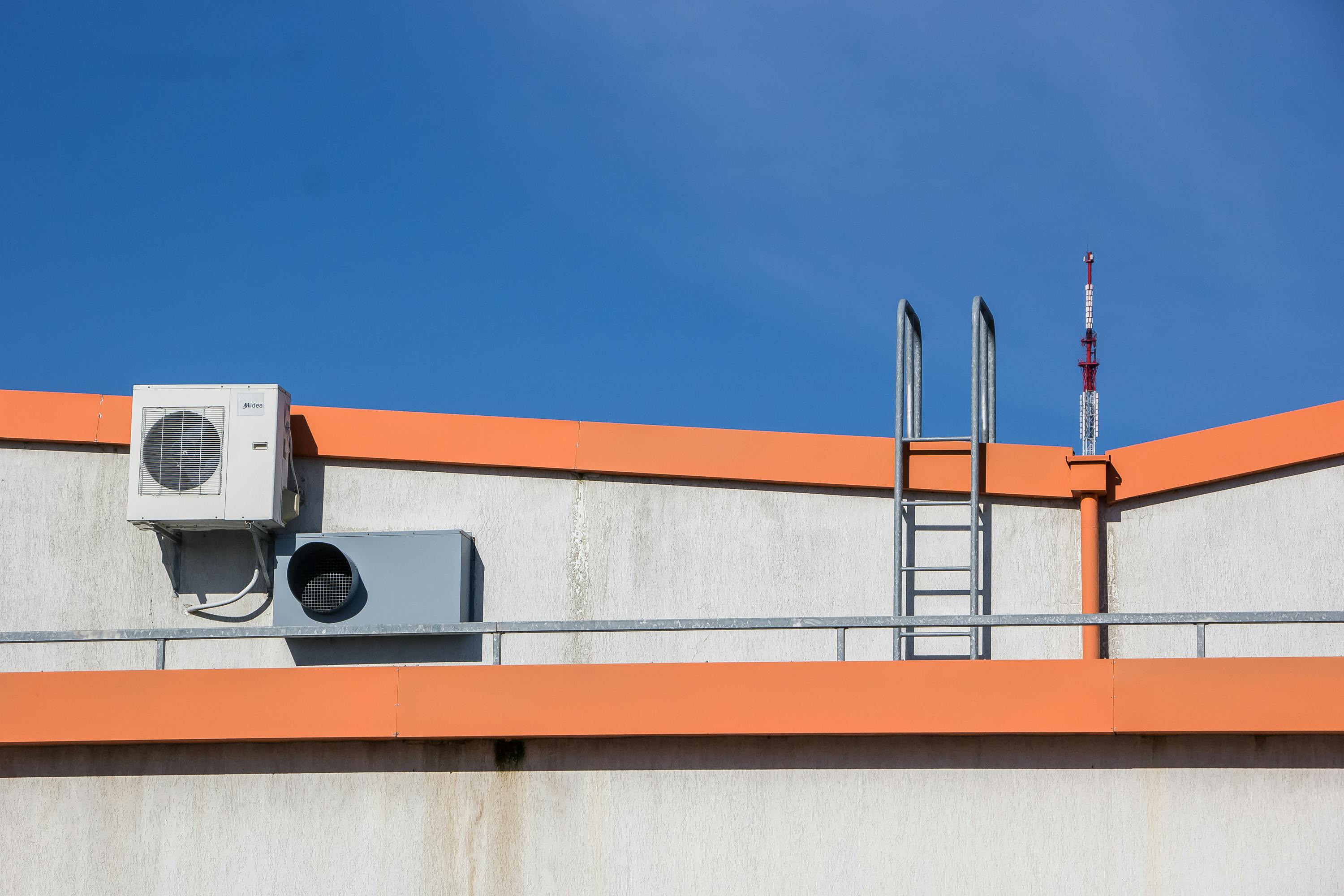 Rooftop HVAC unit and ladder against a clear blue sky.